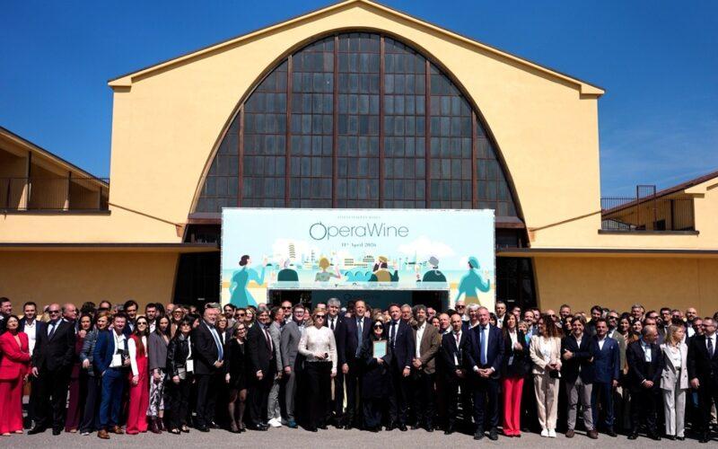 Vinitaly OperaWine: un gruppo di produttori di vino italiani posa davanti a un edificio giallo.