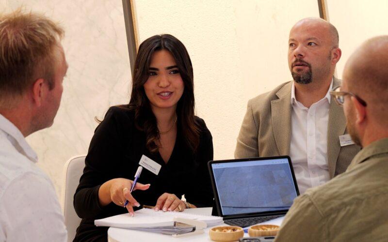 Persone al Marmomac discutono di pietra naturale con brochure e laptop.