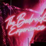 Neon "The Bedrock Experience" sign against a vibrant pink rock background.