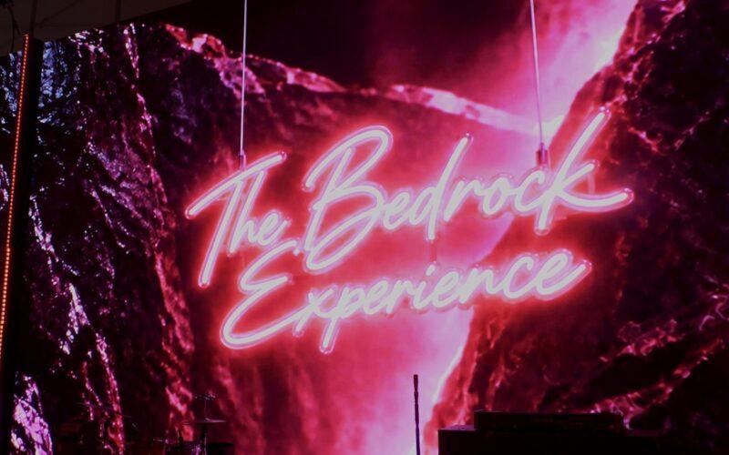 Neon "The Bedrock Experience" sign against a vibrant pink rock background.
